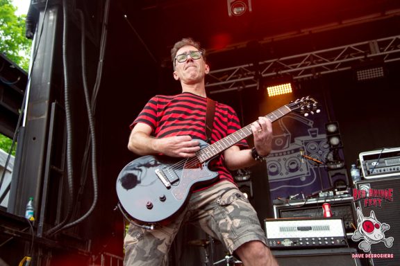 A musician in a striped shirt playing guitar on stage during a performance.