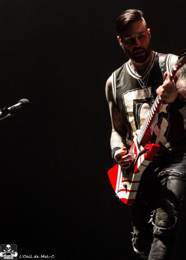 Musician playing a red electric guitar on stage with dramatic lighting.