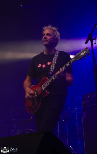A musician playing guitar on stage with purple lighting.