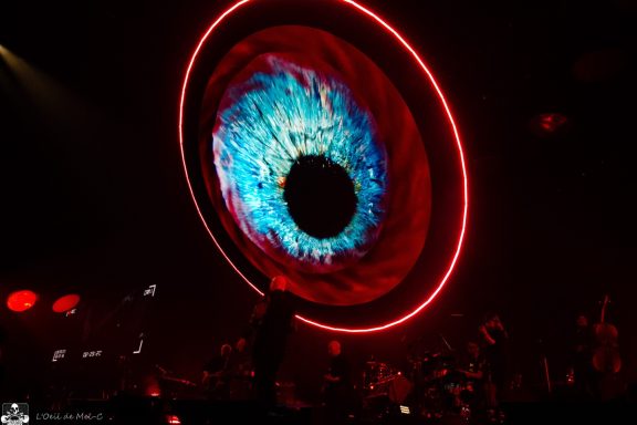 Concert scene with a large, colorful eye graphic in the background.