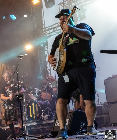 A musician playing a banjo on stage with a band in the background.