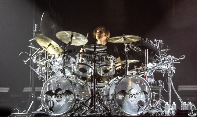 Drummer performing on stage with a dynamic setup and intense lighting.