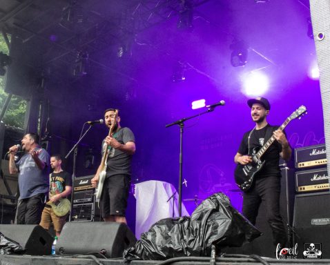 Band performing on stage with instruments and colorful lighting.