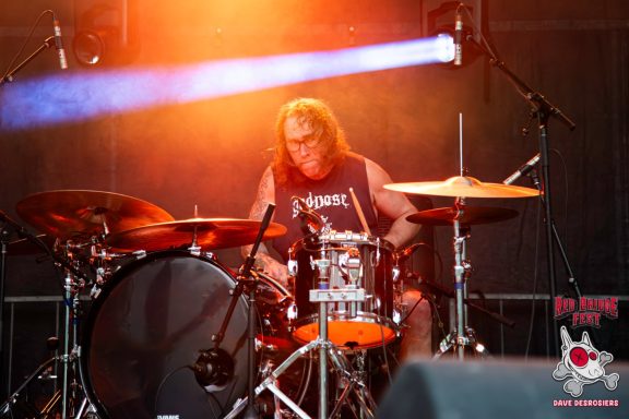 Drummer performing on stage under vibrant lighting.
