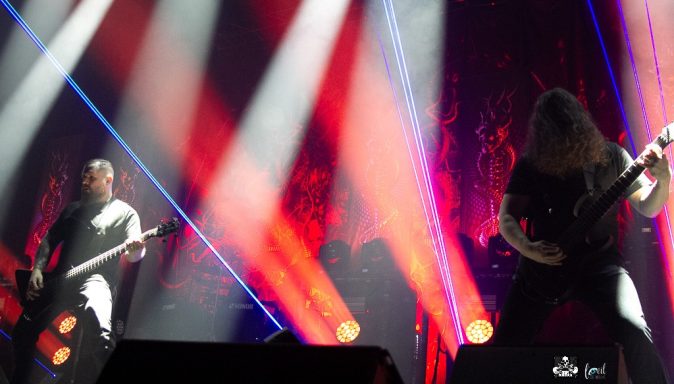 Two musicians performing on stage with dramatic lighting and lasers.