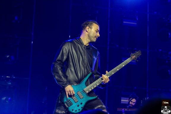 Musician playing a blue bass guitar on stage with blue lighting.