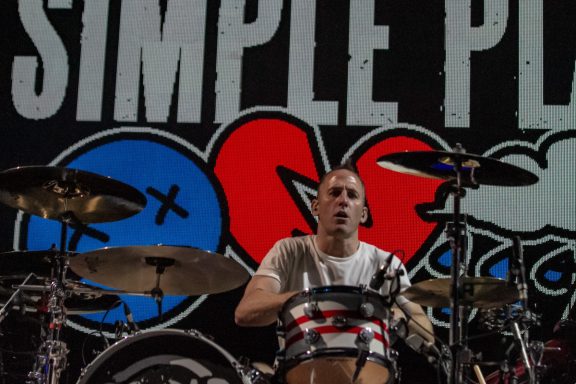 Drummer performing on stage with a Simple Plan backdrop.