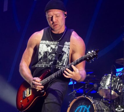 Musician performing on stage, playing an electric guitar with focused expression.