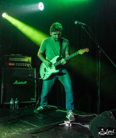A guitarist performing on stage under green light.