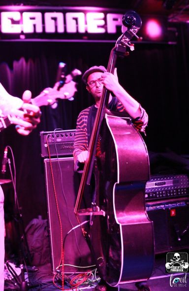 Musician playing double bass on stage with purple lighting in the background.