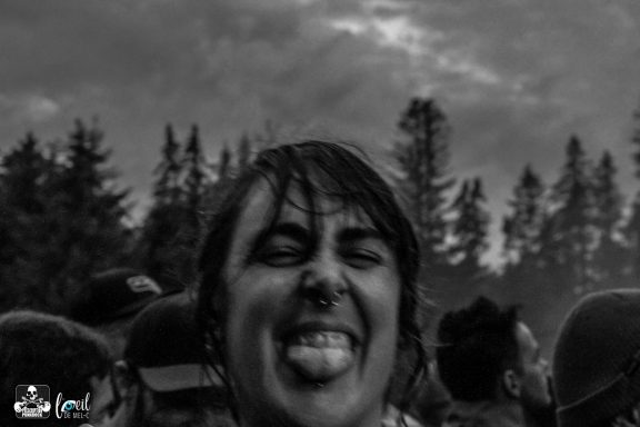 Person making a funny face and sticking out their tongue, surrounded by trees and a cloudy sky.