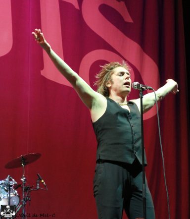 A performer stands on stage with arms outstretched, singing passionately.