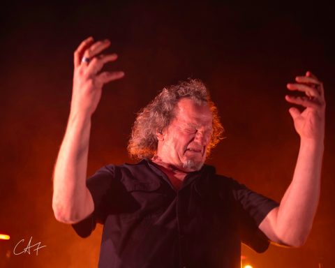 Man performing on stage with raised hands, illuminated by warm lighting.