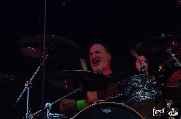 Drummer performing energetically on stage, smiling while playing the drums.