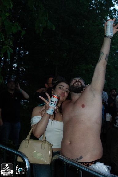 Two people celebrating at a party, one shirtless, holding drinks and smiling.