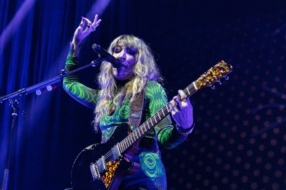 The Damn Truth - Centre Videotron Musician with long hair in a green patterned outfit plays guitar and sings on stage.