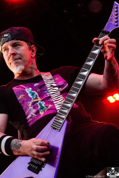 Musician playing a purple guitar, wearing a black t-shirt with a vibrant graphic design.