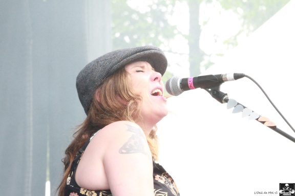 Singer performing on stage, wearing a hat and singing into a microphone.