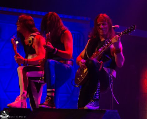 Three musicians performing on stage with electric guitar and lively expressions.