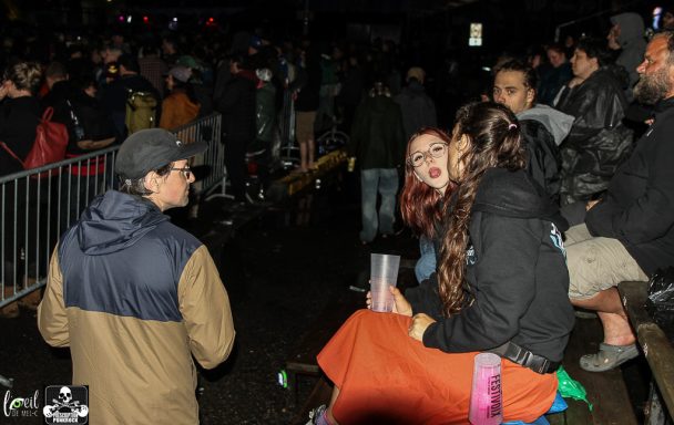 Crowd at night with people sitting and talking, some holding drinks.