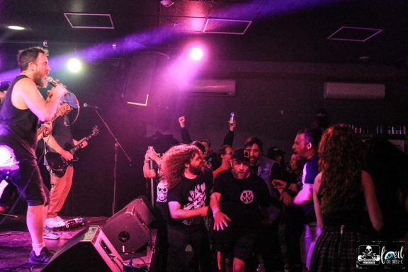 A band performing on stage with an energetic crowd in a dimly lit venue.