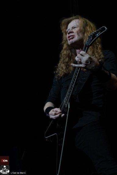 A musician with long hair passionately plays an electric guitar on stage.