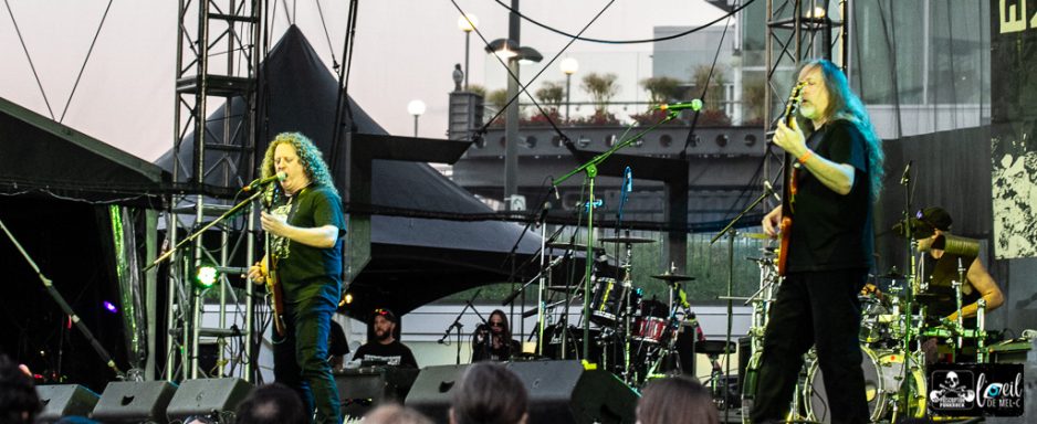 Musicians performing on stage with instruments and a crowd in the background.