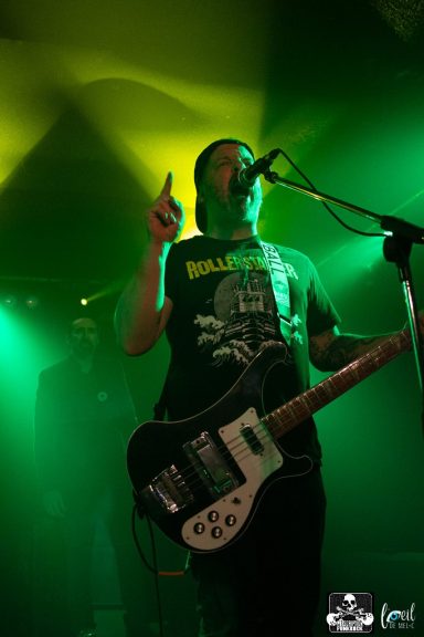 Musician performing on stage with a guitar and singing, illuminated by green lights.