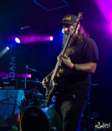 Musician playing bass guitar on stage with colorful lights in the background.