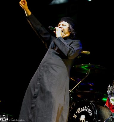 Frontman in a black outfit singing passionately on stage with a raised arm.