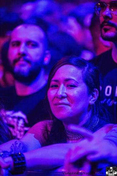 A concert crowd with a woman smiling in front, surrounded by purple lighting.