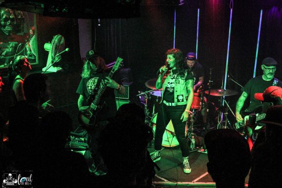 A lively rock band performs on stage with vibrant lighting and energetic crowd.