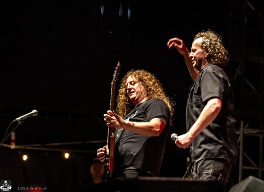 Two musicians perform on stage, one playing guitar while the other sings.