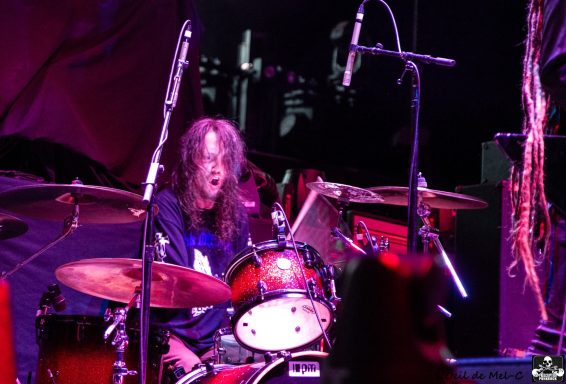 Drummer performing on stage with a vibrant setup and colorful lighting.