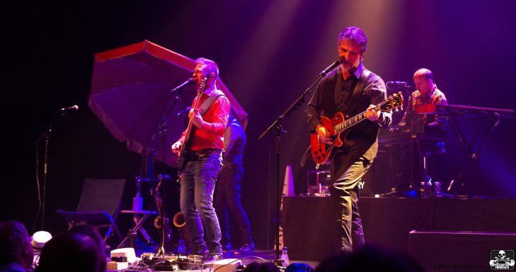 A band performs on stage with vibrant lighting and instruments at a live concert.