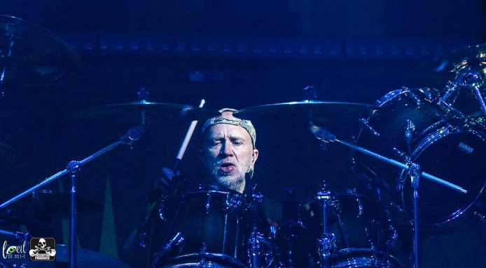 Drummer performing on stage, focused and surrounded by drums and cymbals.