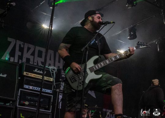 A musician playing guitar on stage during a performance, wearing a black cap and shirt.