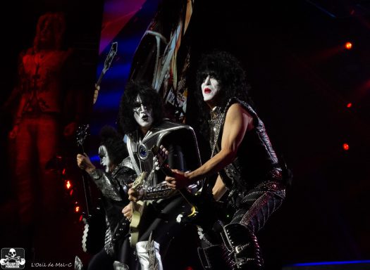 Performance by band members in elaborate costumes and face paint, surrounded by dramatic lighting.