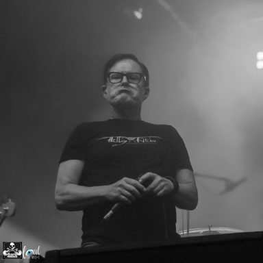 A musician with glasses and a black shirt performs on stage with a microphone.