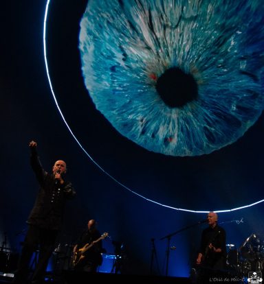 A performer on stage with a large, artistic eye graphic in the background.