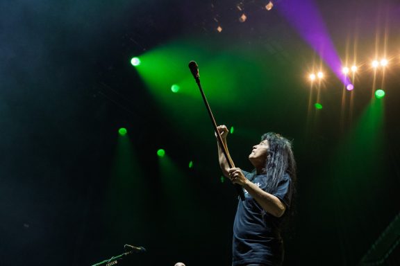 Performer holding a microphone with vibrant stage lighting in the background.