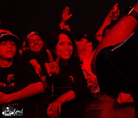 Crowd at a concert, with a woman making a rock gesture and people cheering around her.