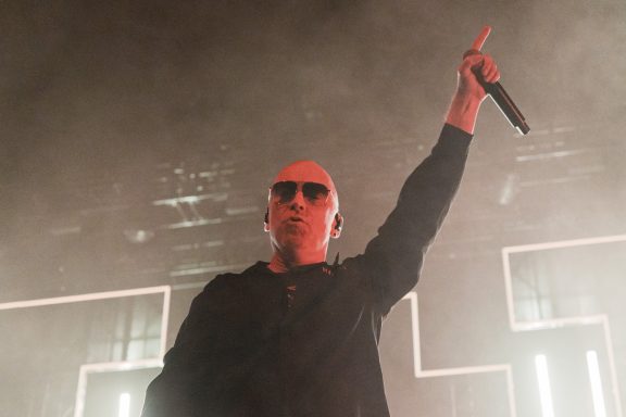 +LIVE+ - Centre Videotron A performer with sunglasses raises a microphone on stage, illuminated by red lighting.