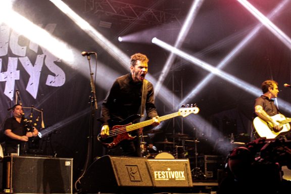 Band performing on stage with bright lights, featuring a bassist and guitarist.