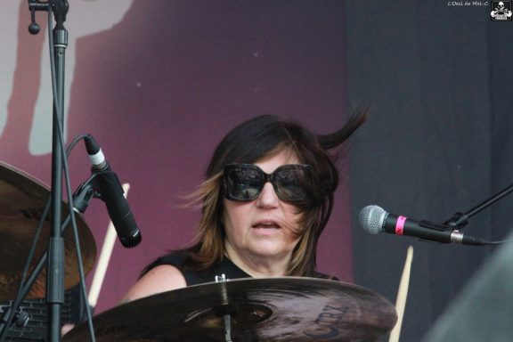 Drummer wearing sunglasses, focused on playing with long hair flowing.