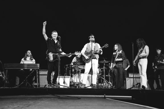A band performing on stage with various instruments and musicians in black and white.