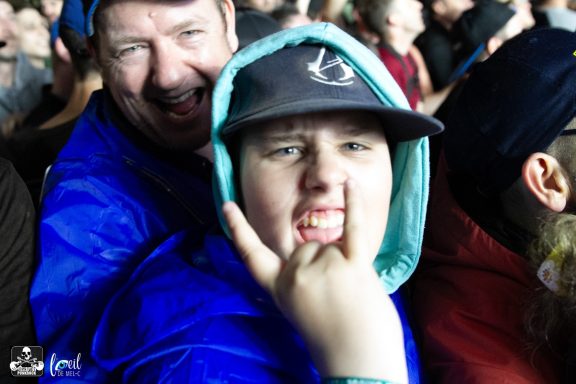 Two people at a concert; one man smiles while a boy makes a rock hand gesture.