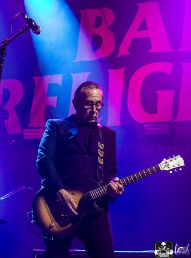 Musician playing electric guitar on stage with colorful lighting backdrop.