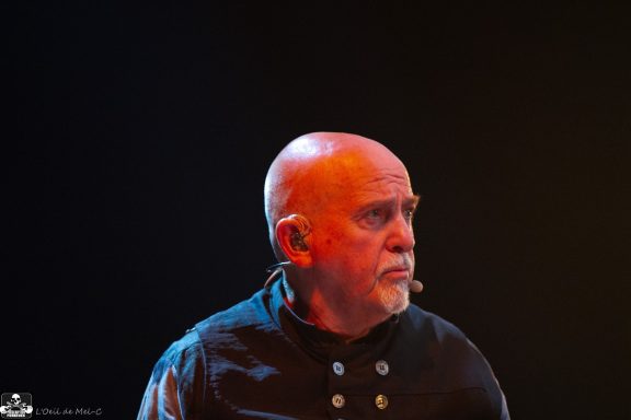 A man with a shaved head and goatee, wearing a black shirt, looks thoughtfully.