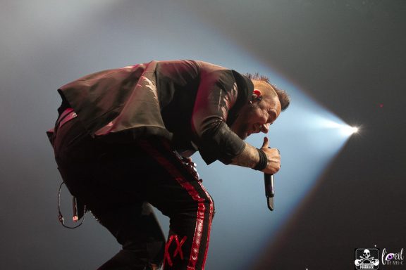 Musician performing energetically on stage with microphone, spotlight shining.